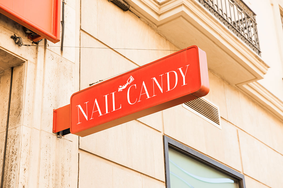 An outdoor sign jutting out from a building that says Nail Candy.