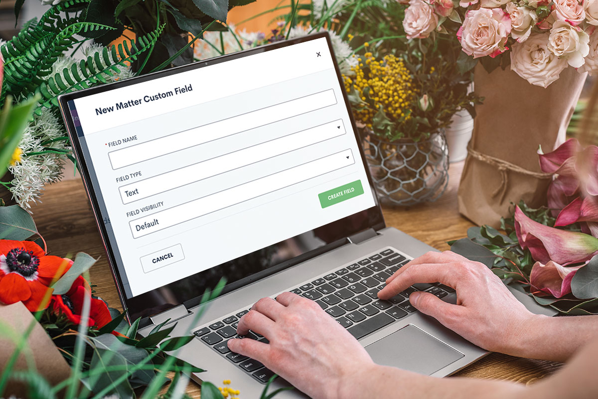 A business owner typing their business name into a laptop on a desk covered with flowers and plants.