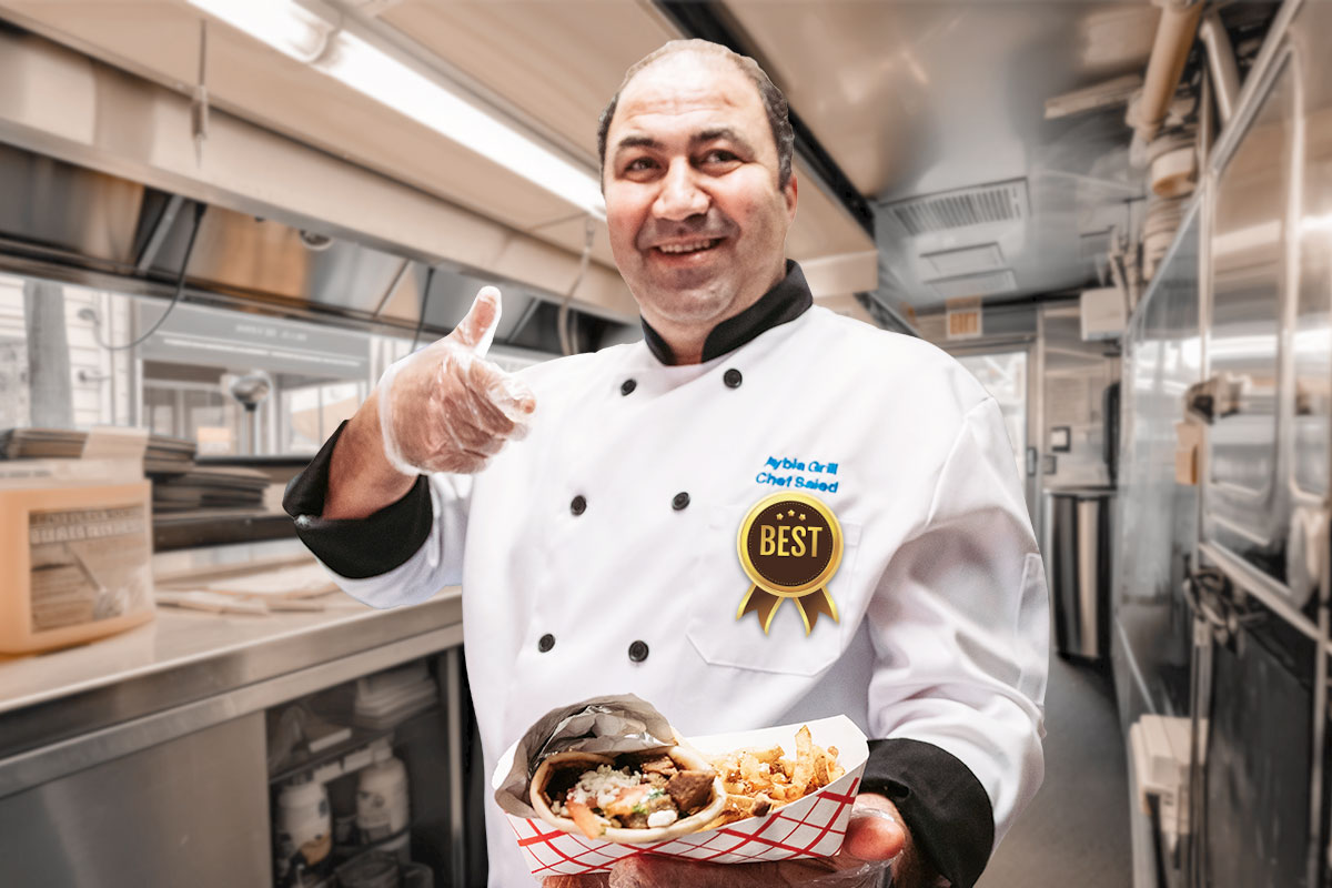 The owner of Aybla Grill holding a to-go order while working inside a food truck.