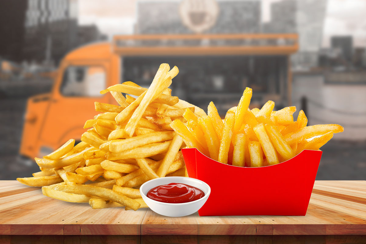 A large serving of french fries with ketchup sitting on a table with a food truck in the background.