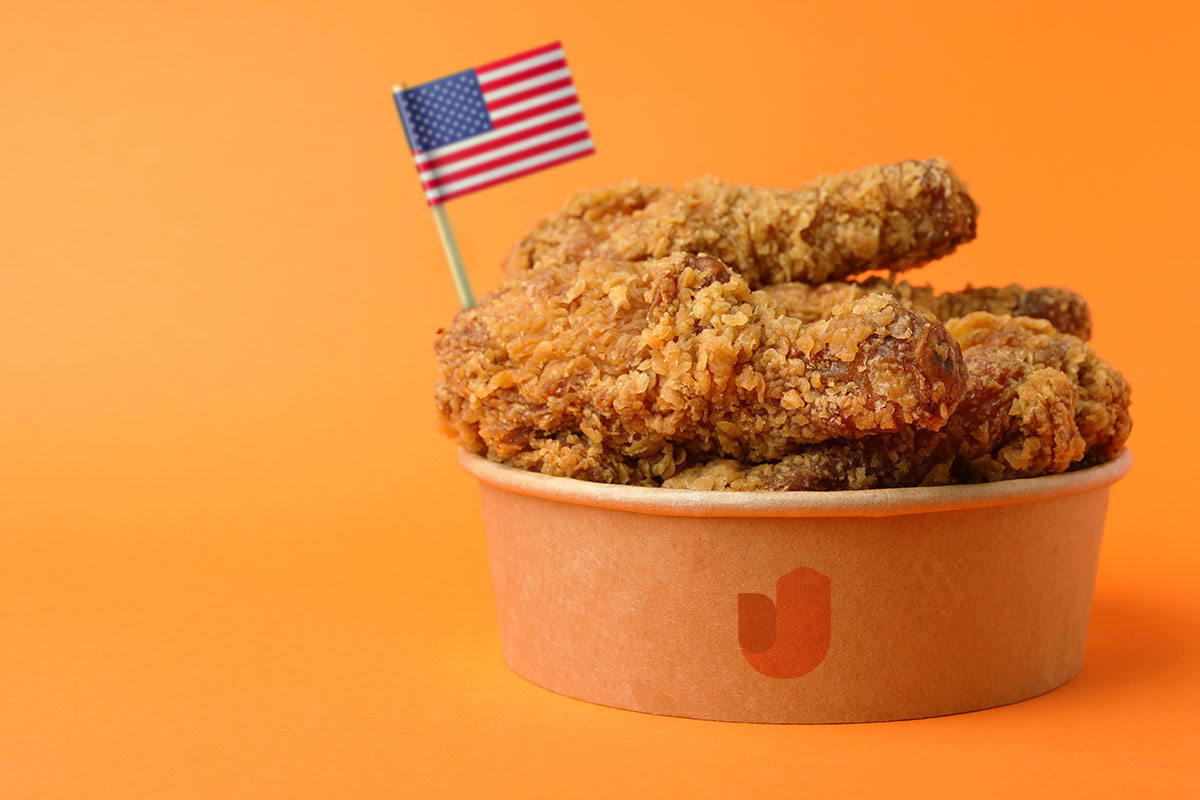 A to-go container full of fried chicken with an American flag on a toothpick sticking out from the top.