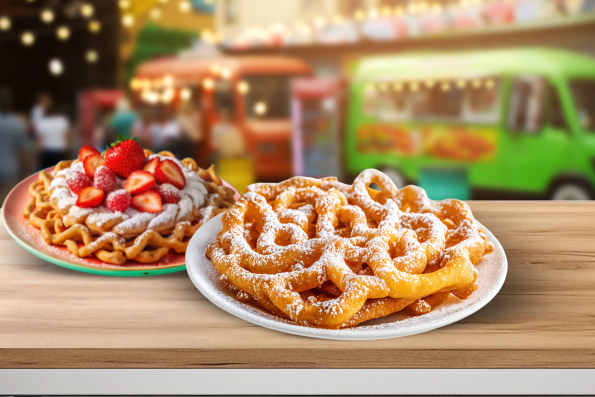 Two funnel cakes sitting on a table with carnival-themed food trucks in the background.