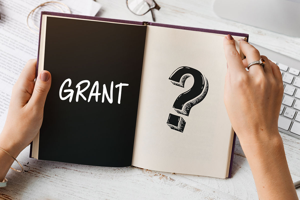 Grants 101 for Small Business Owners 82 A businesswoman looking at a book with the word grant on one side and a question mark on the other.