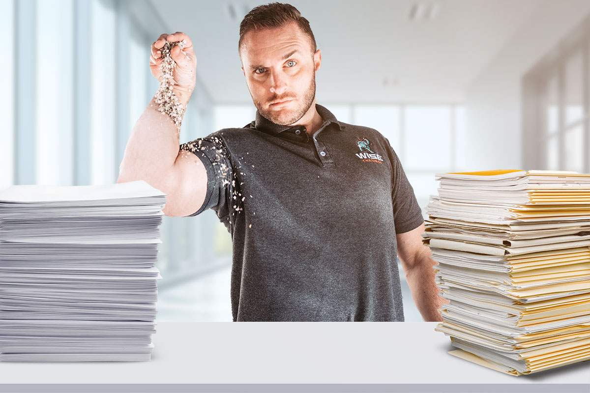 Small Business Marketing 13 The owner of Wise Coatings standing behind a desk with two stacks of folders and paperwork.