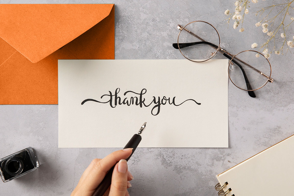 Business Thank You Messages to Customers 11 A thank you note written in calligraphy sitting on a desk next to a pair of eyeglasses and an envelope.