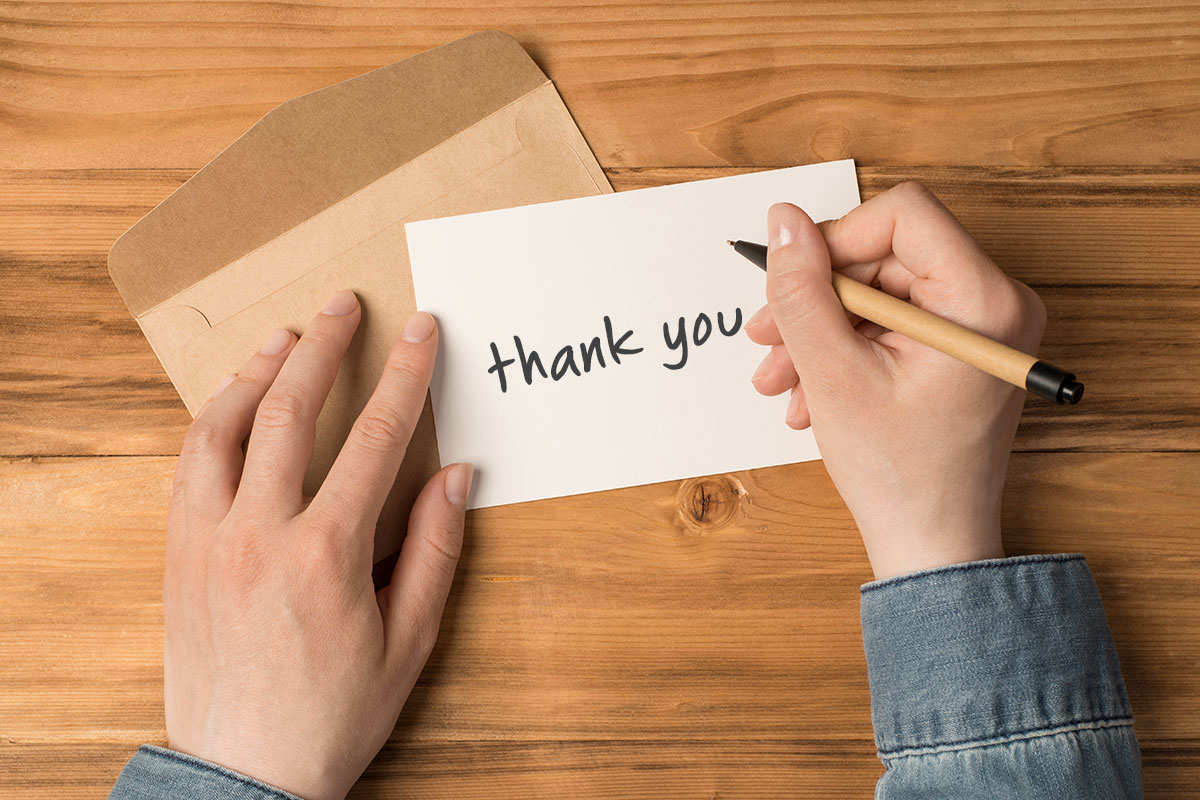 Business Thank You Messages to Customers 9 A person writing a thank you note on top of a wooden desk.
