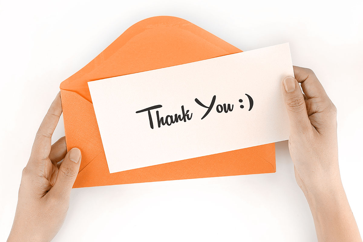Business Thank You Messages to Customers 2 An open orange envelope and a typed thank you note with a smile emoji.