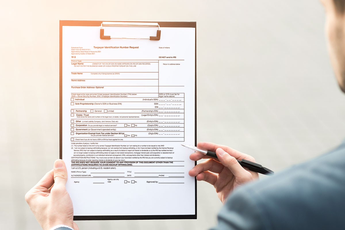 A business owner filling out a taxpayer identification number request form on a clipboard.